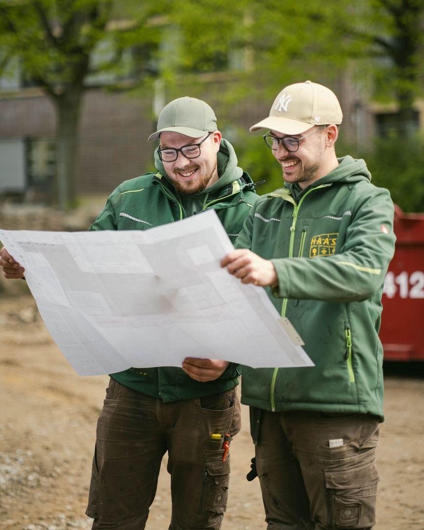 Zwei Mitarbeiter besprechen einen Lageplan in der Natur